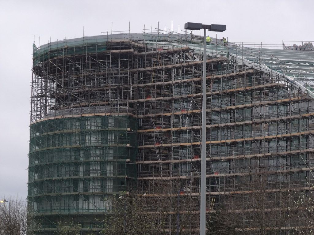 A large residential building under construction behind scaffolding, with a street lamp in the foreground